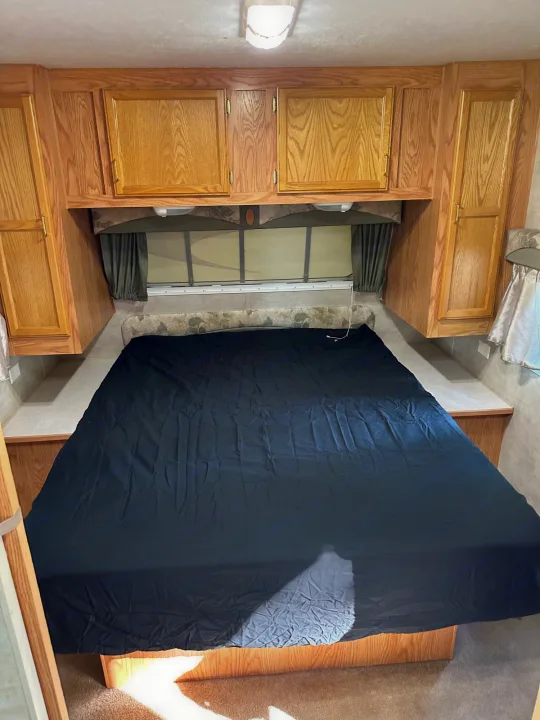 Cozy RV rental bedroom with a large bed, overhead wood cabinets, and a window for comfortable travel.. Jayco Jay Flight 2003