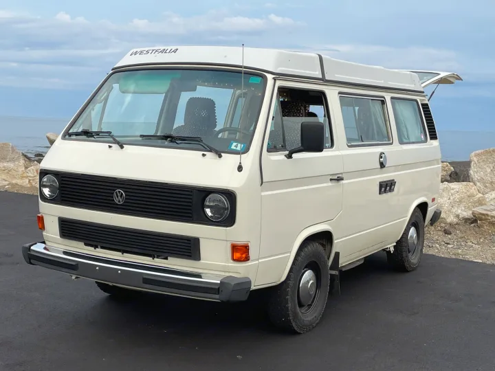 A cream VW Westfalia camper van, ready for rv rental road trips. Parked seaside with rear hatch open.. Volkswagen Westfalia 1983