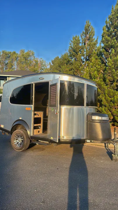 Stylish silver travel trailer RV rental parked on asphalt with its door open, ready for adventure.. Airstream Base Camp 2021
