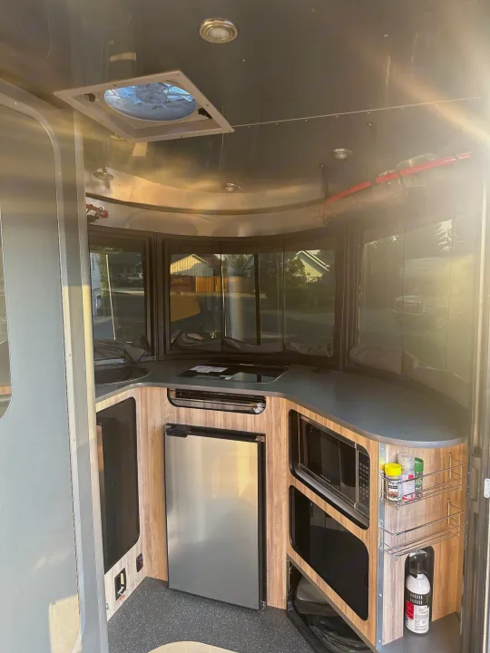 Inside a modern rv rental: compact kitchen with sink, cooktop, fridge, and microwave. Bright, ready for travel.. Airstream Base Camp 2021
