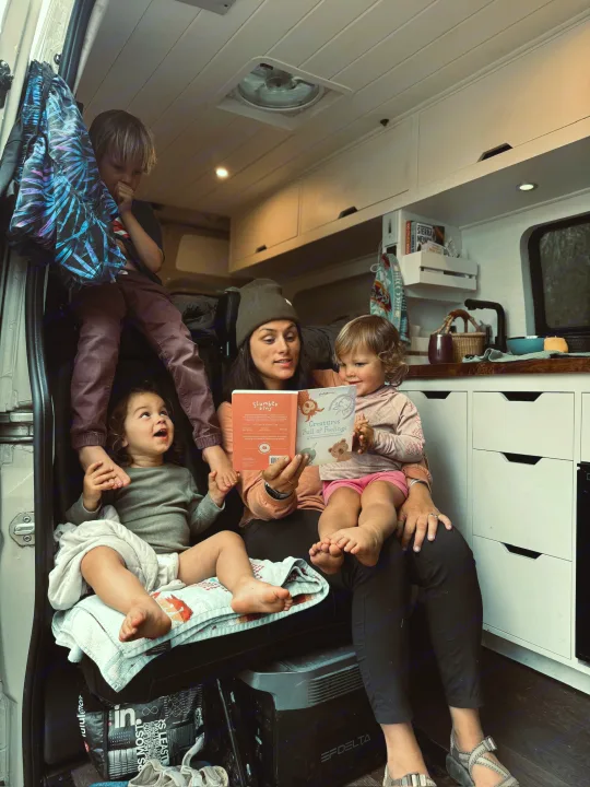 Cozy rv rental family time! Mom reads "Creatures Full of Feelings" to kids in their camper van, a perfect travel moment.. Mercedes-Benz Sprinter 2020