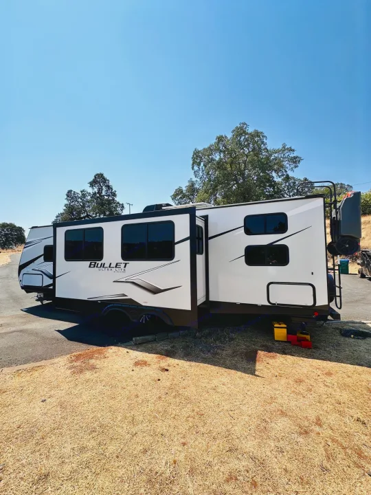 Explore with this white Bullet travel trailer RV rental, extended and parked outdoors. Ideal for your next camper adventure.. Keystone RV Bullet Ultra Lite 2023