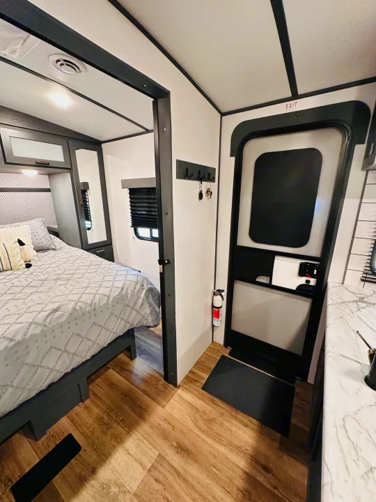 Modern RV rental interior: bedroom, main entry door with fire extinguisher, and a glimpse of the kitchen. Ready for your trip.. Keystone RV Bullet Ultra Lite 2023