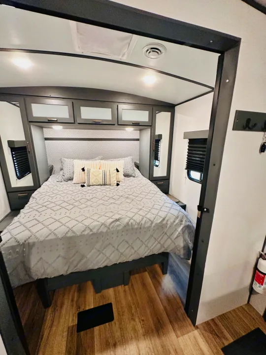 Relaxing RV rental bedroom with a comfy bed, overhead cabinets, and stylish gray & white decor.. Keystone RV Bullet Ultra Lite 2023