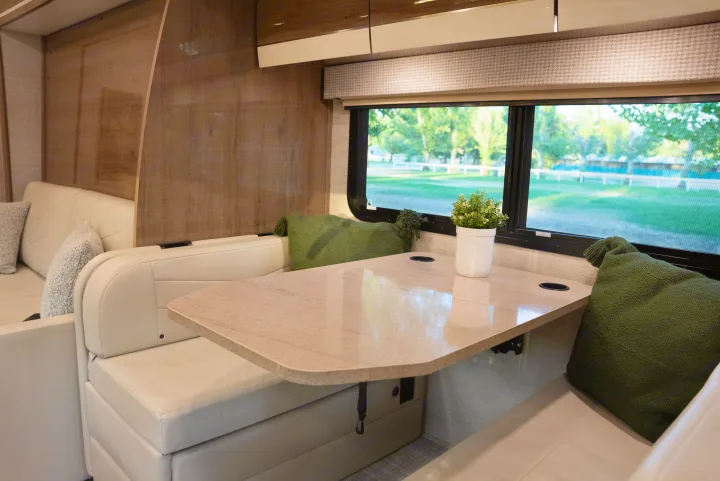 RV rental dinette interior: light beige bench seating, green pillows, and a table by a window with a green outdoor view.. Entegra Coach Other 2023