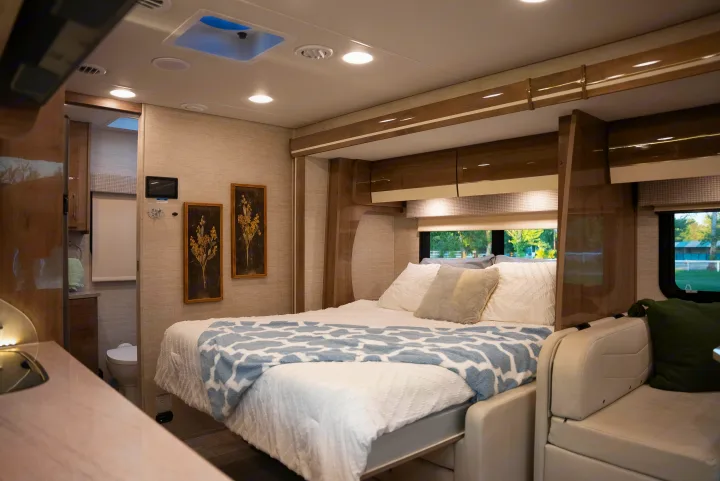 Cozy RV rental bedroom featuring a comfortable bed with pillows, overhead storage, and a glimpse of the compact bathroom.. Entegra Coach Other 2023