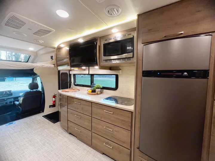 Modern RV rental kitchen featuring a fridge, microwave, cooktop, and TV. A compact, functional living space.. Entegra Coach Other 2023