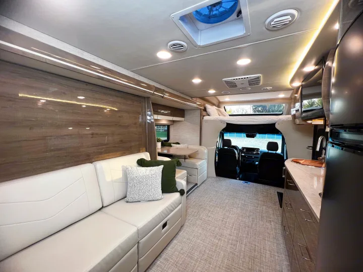 Bright, modern RV rental interior with cream sofa, dining booth, kitchen, and overhead bunk. Ready for your adventure!. Entegra Coach Other 2023