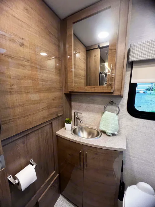 RV rental: Glossy wood-look bathroom with a vanity, stainless steel sink, mirror, toilet, and compact setup.. Entegra Coach Other 2023