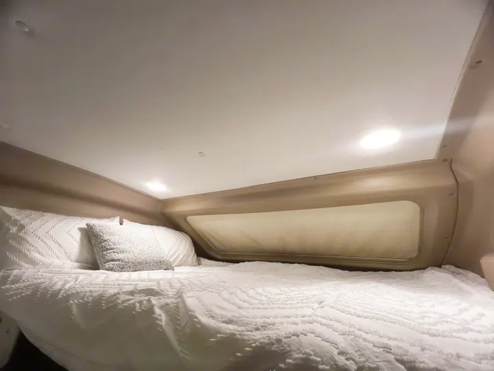Experience comfort in this cozy RV rental sleeping nook. White bedding, pillows, and soft lighting create a peaceful retreat.. Entegra Coach Other 2023