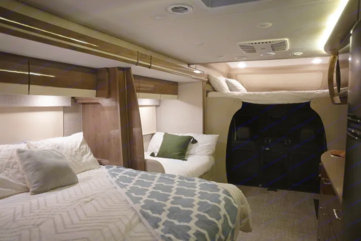 Cozy rv rental sleeping area with a main bed and an overhead bunk. Modern interior with warm lighting and wood accents.. Entegra Coach Other 2023