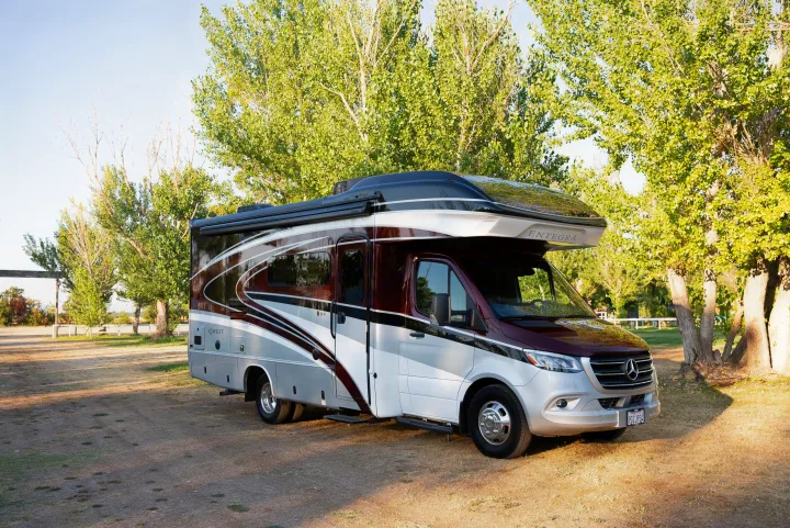 Maroon and silver Entegra QWEST Class C RV rental, parked on dirt under green trees. Ready for comfortable exploration.. Entegra Coach Other 2023