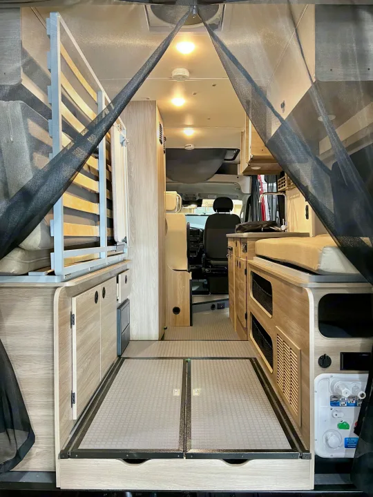 RV rental: Interior of a camper van with a bed/seating area, storage, and kitchen, viewed through a protective bug net.. Winnebago Solis 2023