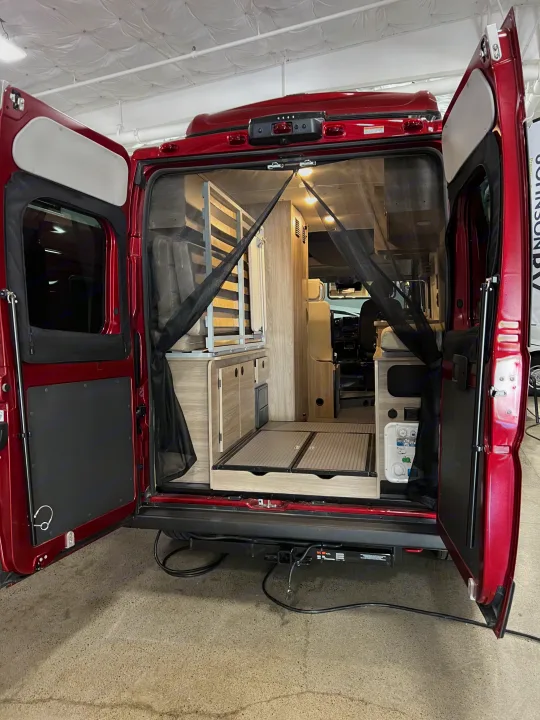 Experience adventure with this RV rental! Rear view of a red camper van interior, showcasing compact living space, cabinetry, and a mosquito net.. Winnebago Solis 2023