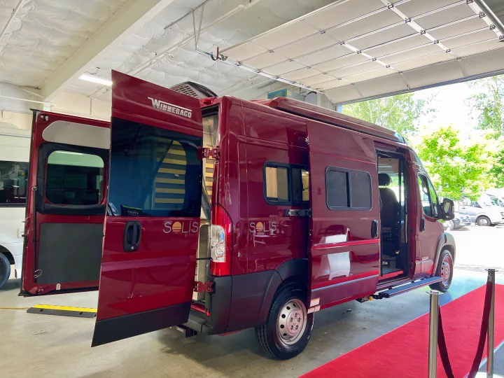 This red Winnebago Solis RV rental van is showcased on a red carpet with all doors open.. Winnebago Solis 2023