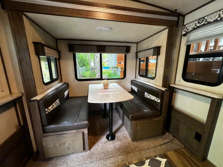 Inside an RV rental: a cozy dinette with dark upholstered benches and a table, framed by windows showing an outdoor scene.. Cruiser Rv Corp Other 2018