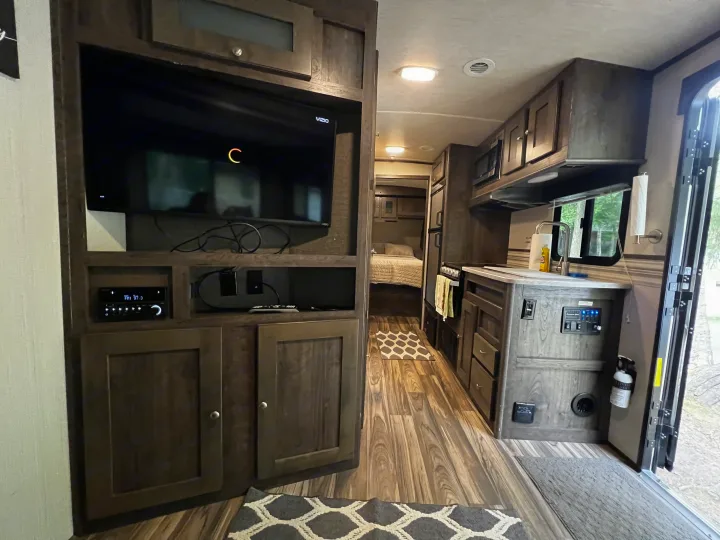 Spacious RV rental interior with wood cabinetry, featuring a living area with TV, full kitchen, and bedroom hallway.. Cruiser Rv Corp Other 2018