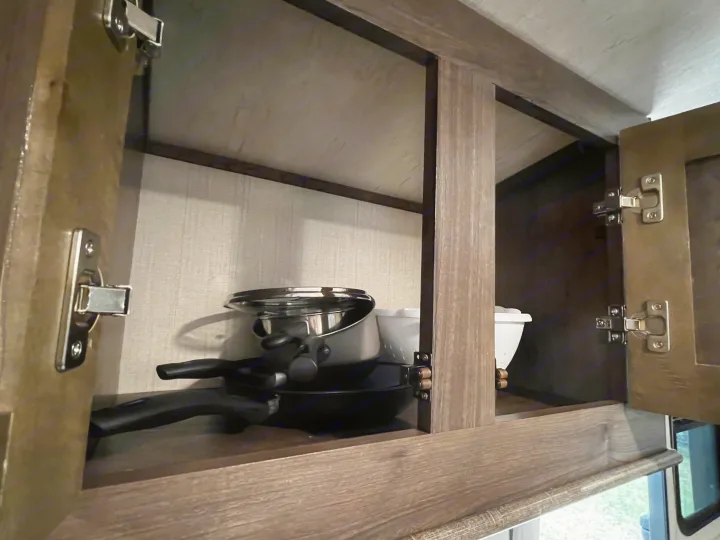 Open kitchen cabinet in an RV rental, showing a pot, pan, and secure latches for travel.. Cruiser Rv Corp Other 2018