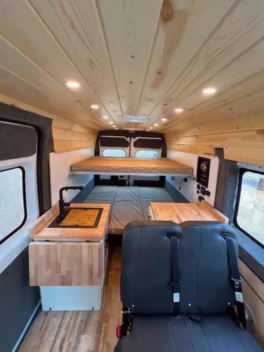 Inside an **rv rental**: cozy wooden interior with multiple beds, kitchenette, and passenger seating.. Ram Promaster 2500 2021