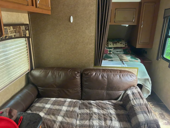 RV rental interior: a comfy brown sofa with a plaid blanket, leading to a cozy bunk bed area with a patterned quilt.. Starcraft Autumn Ridge 2014