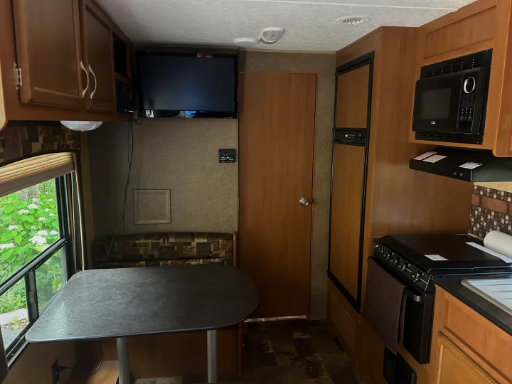 RV rental interior: a functional kitchen with microwave, stove, and fridge, plus a dining area with table and seating.. Starcraft Autumn Ridge 2014