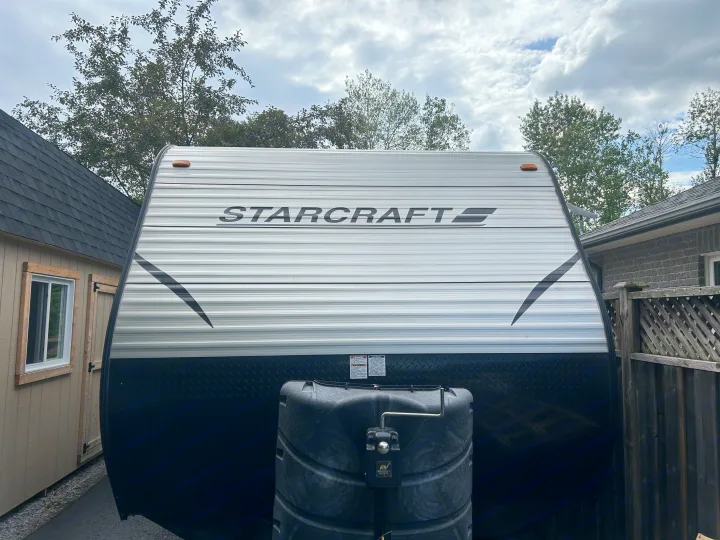 Front of a Starcraft travel trailer, ready for your next rv rental. Features white ribbed siding, black diamond plate, and covered propane tank.. Starcraft Autumn Ridge 2014
