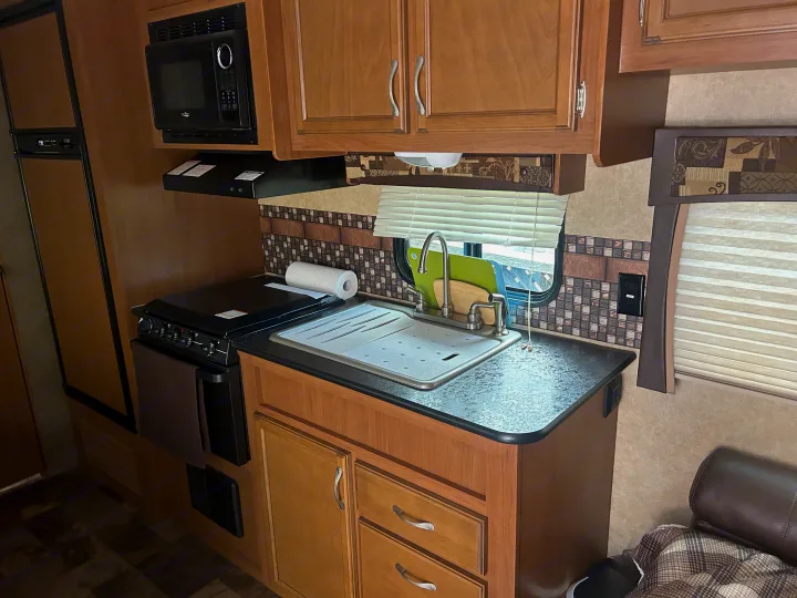 A compact rv rental kitchen featuring a microwave, stove, sink, and wood cabinets, designed for efficiency on the go.. Starcraft Autumn Ridge 2014