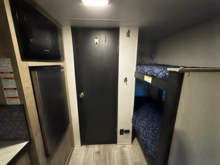 This RV rental interior showcases a compact kitchenette with microwave and fridge, a door, and bunk beds.. Cruiser RV Avenir 2024