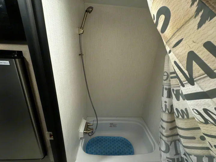 Inside an rv rental: a compact RV bathroom featuring a shower, small tub with blue mat, and a fridge nearby.. Cruiser RV Avenir 2024