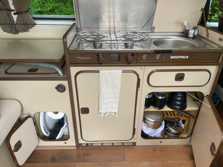RV rental interior: A compact camper van kitchenette featuring a Westfalia stove, sink, and organized storage.. Volkswagen Westfalia 1983