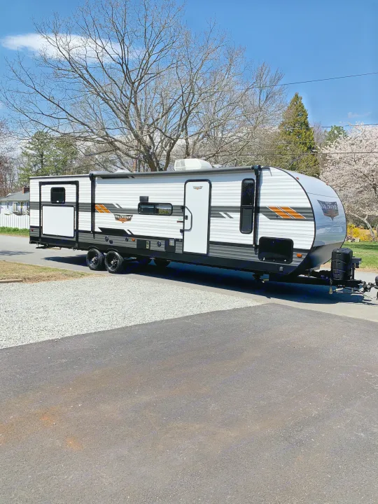 White & black Wildwood travel trailer RV rental, ready for adventure under a blue sky. Ideal for a family trip.. Forest River Wildwood 2021