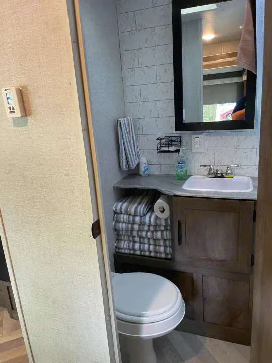 Compact RV rental bathroom with toilet, sink, vanity, mirror, and neatly stacked towels.. Forest River Wildwood 2021