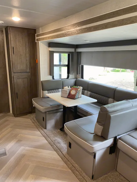 Inside an RV rental, a modern U-shaped dinette with gray seating, light wood-look flooring, and storage cabinets.. Forest River Wildwood 2021