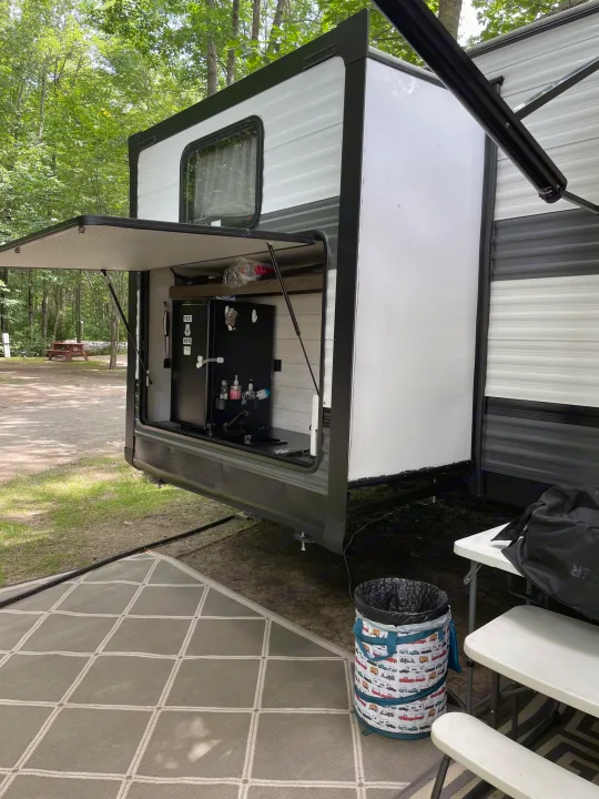 An RV rental's outdoor kitchen, complete with fridge & sink, offers convenient campsite amenities for comfortable camping.. Forest River Wildwood 2021