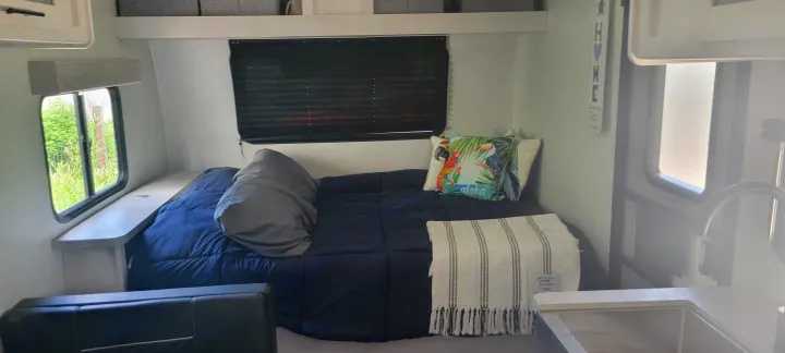 Cozy RV rental bedroom with tropical pillows & blackout blinds. Features a handy shelf & compact kitchen sink.. Dutchmen Coleman Rubicon 2021