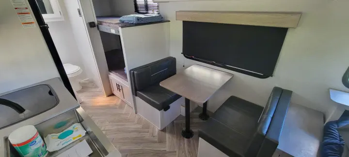 Light-toned RV rental interior featuring bunk beds, a dinette, and compact bathroom/kitchen area. Ideal for travelers.. Dutchmen Coleman Rubicon 2021