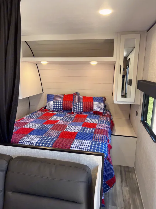Cozy RV rental bedroom with a patriotic quilt, overhead storage, and a window view, offering comfortable mobile living.. Jayco Jay Flight SLX 2024
