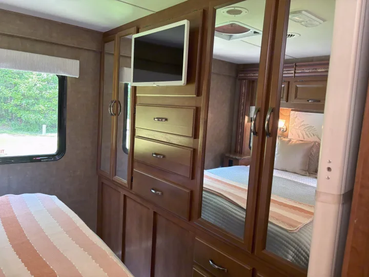 Experience comfort in this RV rental bedroom: striped bed, window view, built-in TV, and mirrored storage.. Thor Four Winds 2014