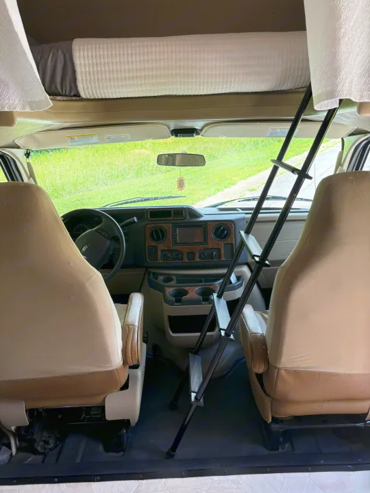 Inside an RV rental: view of the cockpit with dashboard, front seats, and an overhead sleeping bunk with its ladder.. Thor Four Winds 2014