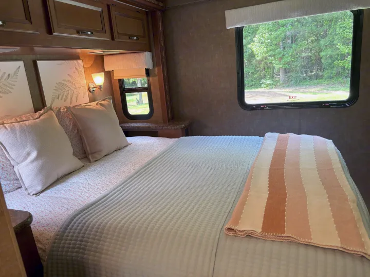 Cozy RV rental bedroom featuring a comfy bed with light bedding, a striped throw, and a window view of nature.. Thor Four Winds 2014