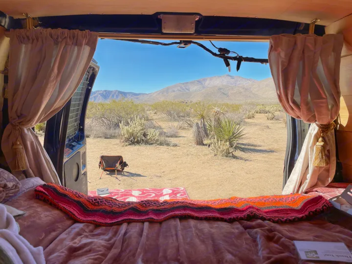 View from a cozy RV rental bed looking out at a serene desert landscape with mountains and cacti. Perfect for camping!. Ford Econoline 2010