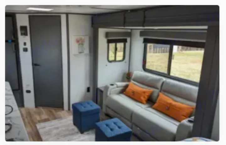 Modern RV rental living space featuring a grey sofa, orange pillows, large windows, & blue ottomans.. Keystone RV Bullet Crossfire 2023