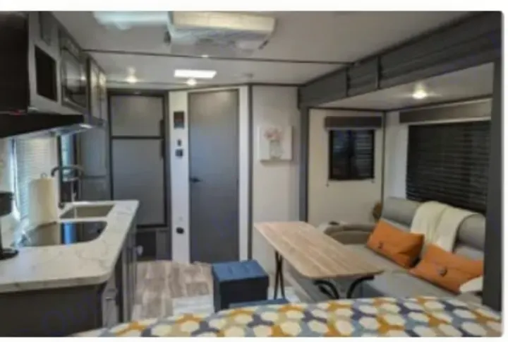 RV rental interior: kitchen on left, central doors, and a living/dining area with table and sofa on the right.. Keystone RV Bullet Crossfire 2023