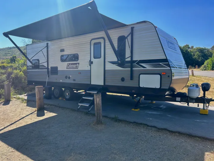 Sunny Coleman RV rental travel trailer fully set up at a campsite, awning extended for a relaxing stay.. Coleman Lantern lt 2023