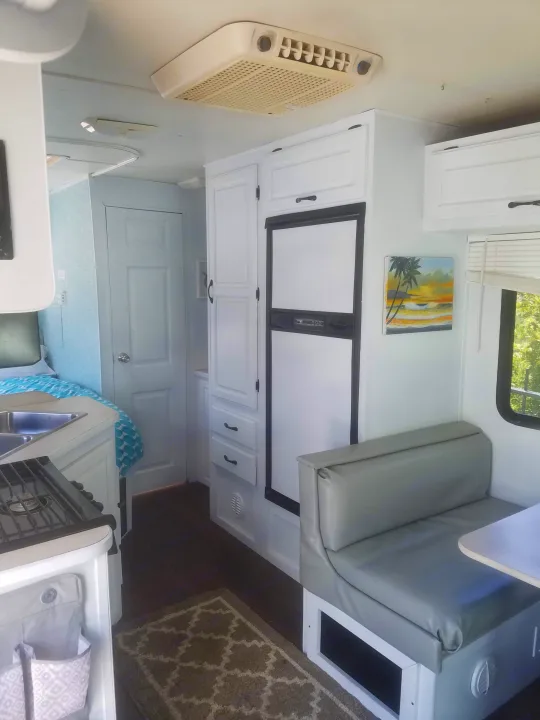 Bright, updated RV rental interior: kitchen with sink/stove, dinette with light gray seating, fridge, and bedroom access.. four winds majestic 2004
