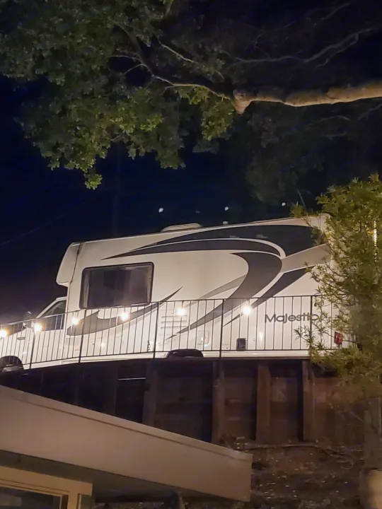 This Majestic RV rental is parked on an elevated deck at night, illuminated by string lights on the railing.. four winds majestic 2004