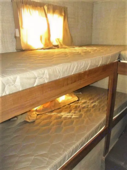 Interior view of an RV rental showing stacked bunk beds with mattresses and a brightly lit window.. Gulf Stream Kingsport 2020
