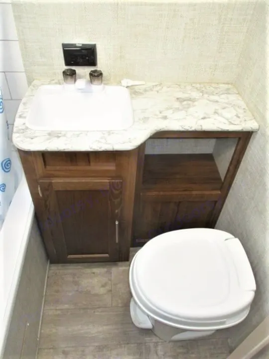 Compact RV rental bathroom with a white sink, wood-look vanity, marble countertop, and toilet.. Gulf Stream Kingsport 2020