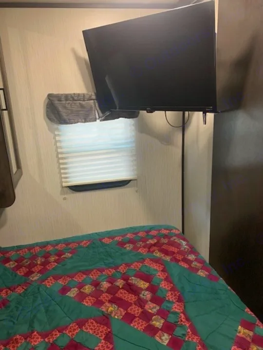 Cozy RV rental bedroom with a quilted bed, window blinds, and wall-mounted TV, ideal for travel.. Heartland RVs Mallard 2021