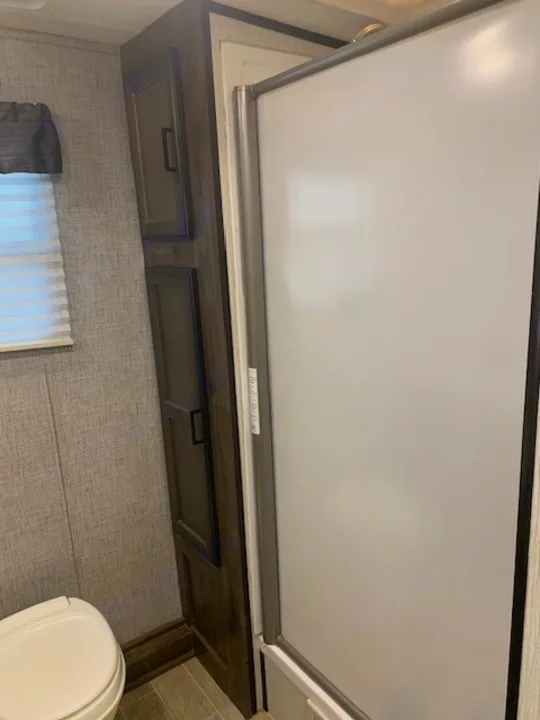 RV rental bathroom featuring a toilet, a tall storage cabinet, and a frosted shower enclosure.. Heartland RVs Mallard 2021